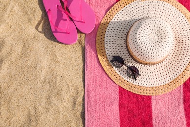 Photo of Beach towel with slippers, straw hat and sunglasses on sand, flat lay. Space for text