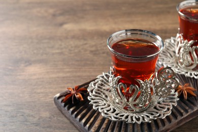 Photo of Glasses of traditional Turkish tea in vintage holders and anise stars on wooden table, closeup. Space for text