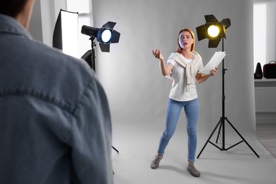 Emotional woman with script performing in front of casting director against grey background at studio