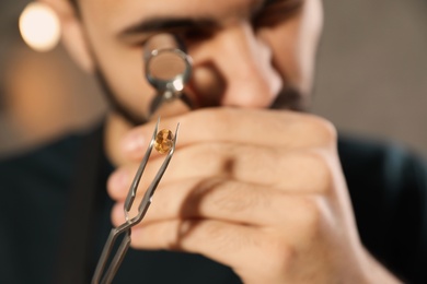 Photo of Male jeweler evaluating precious gemstone in workshop, closeup