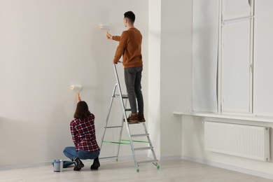 Photo of Young couple painting wall with rollers indoors. Room renovation