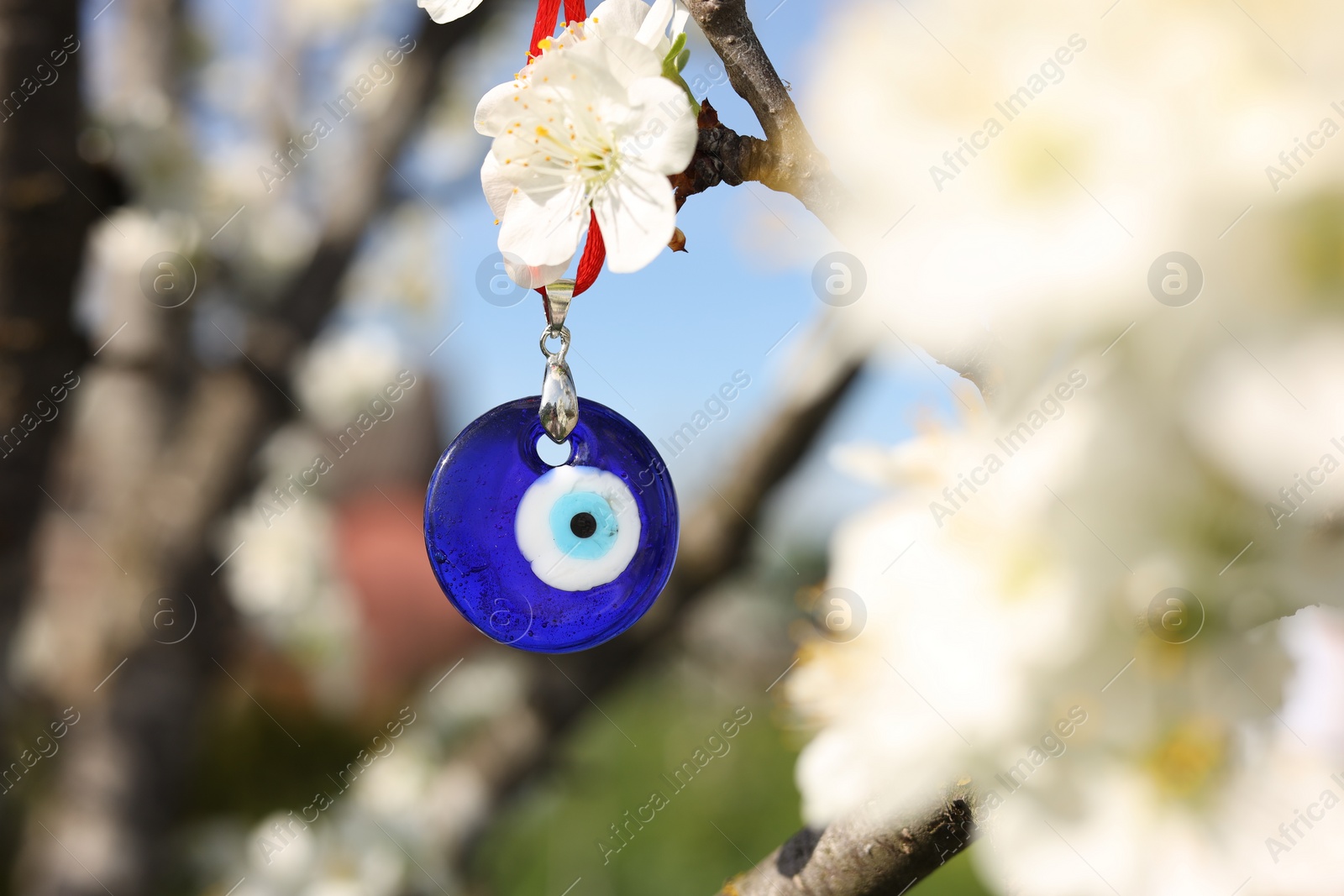 Photo of Evil eye amulet hanging on blossoming spring tree outdoors. Space for text