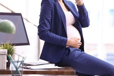 Photo of Young pregnant woman in suit at workplace, closeup