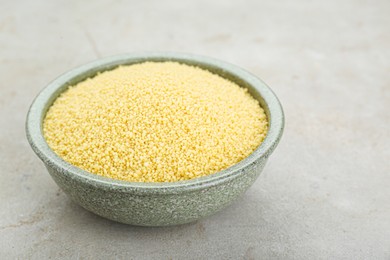 Bowl of raw couscous on light table, closeup