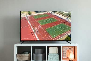 Image of Modern TV set on wooden stand in room. Scene of sport broadcasting