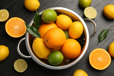 Photo of Fresh citrus fruits in colander on dark textured table, flat lay