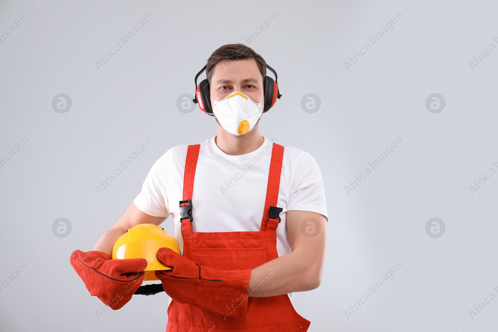 Photo of Male industrial worker in uniform on light background. Safety equipment