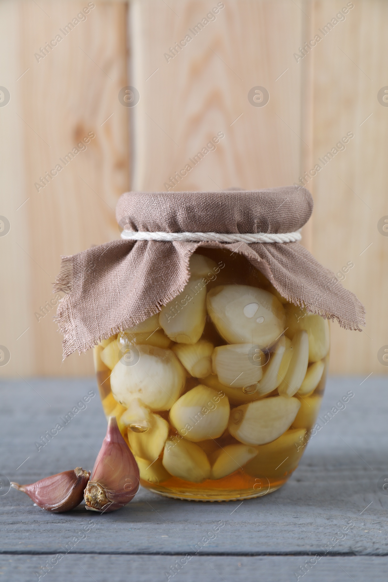 Photo of Garlic with honey in glass jar and unpeeled cloves on grey wooden table