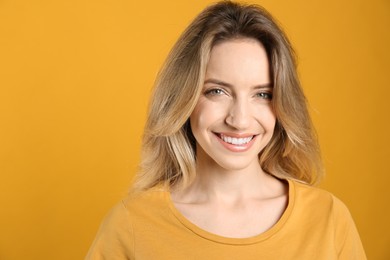 Portrait of happy young woman with beautiful blonde hair and charming smile on yellow background