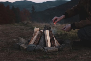 Photo of Traveler lighting up bonfire with matches outdoors in evening, closeup
