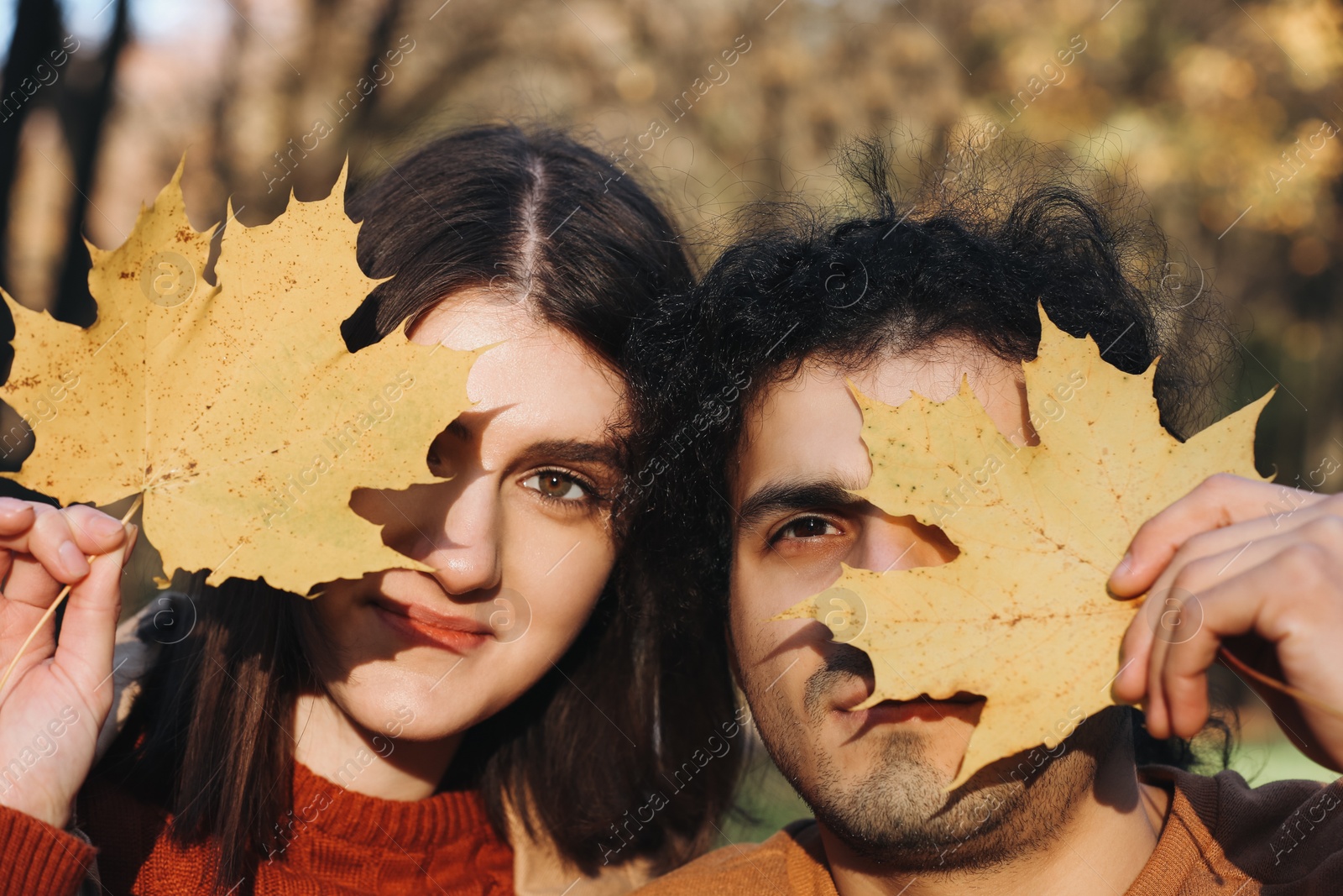 Photo of Young couple holding dry leaves near their faces outdoors. Dating agency