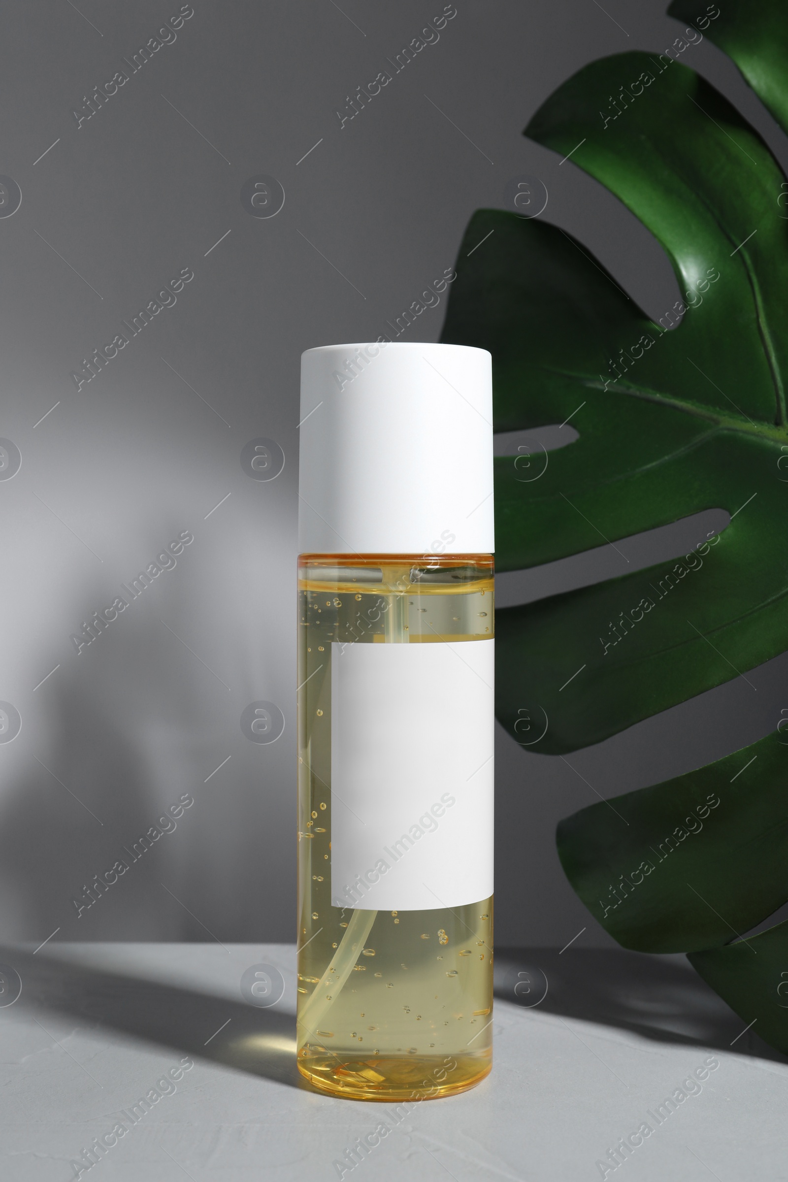 Photo of Bottle of cosmetic product and green palm leaf on table against light background