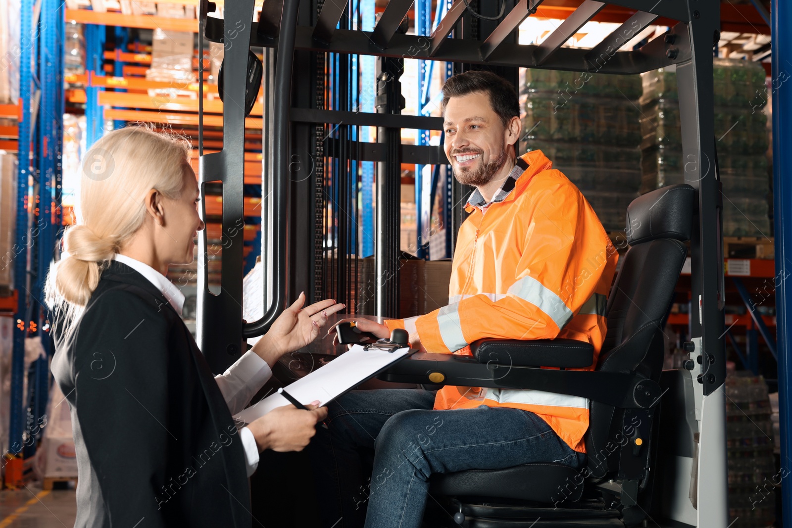 Photo of Happy worker talking with manager while sitting in forklift truck at warehouse