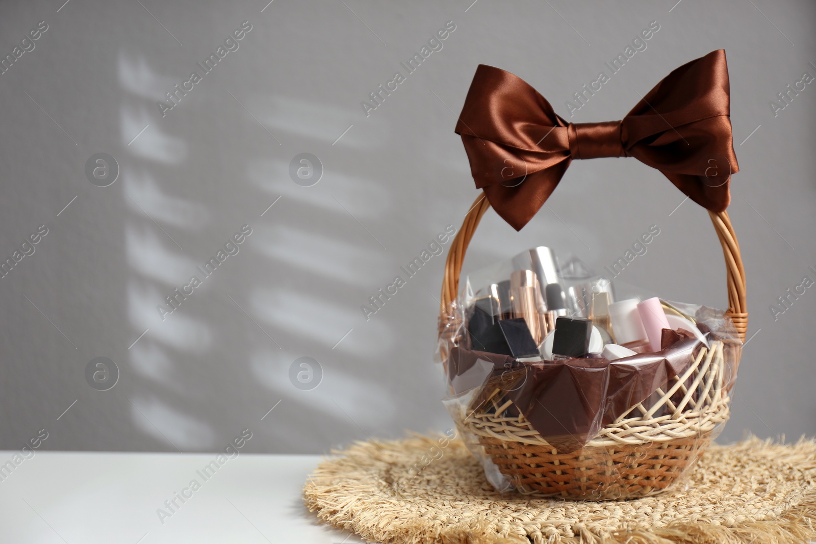 Photo of Wicker gift basket with cosmetic products on white table against grey background. Space for text