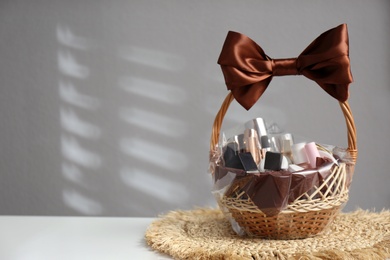 Wicker gift basket with cosmetic products on white table against grey background. Space for text