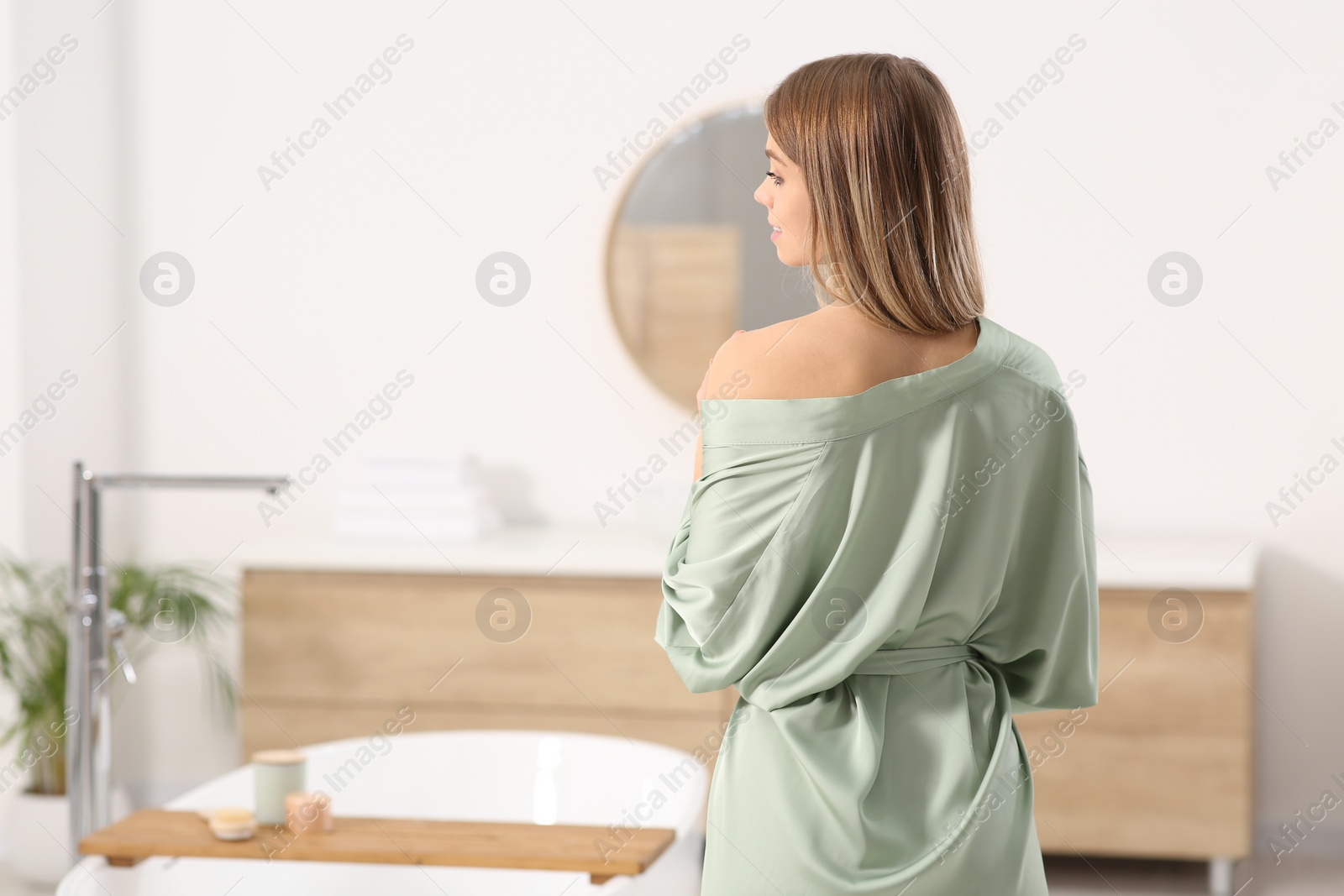 Photo of Woman wearing stylish robe in bathroom, back view. Space for text