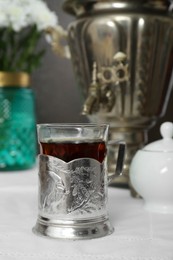 Glass of aromatic tea in vintage holder on table indoors