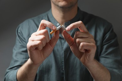Photo of Stop smoking. Man holding broken cigarette on grey background, closeup