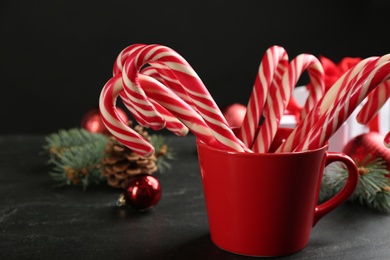Photo of Christmas candy canes in cup on black table, closeup