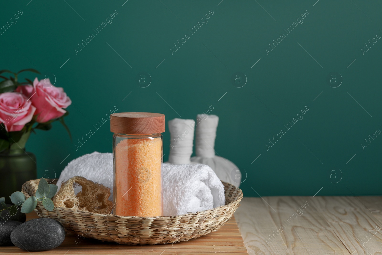 Photo of Beautiful composition with sea salt, roses and different spa products on wooden table near green wall, space for text