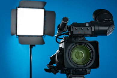 Photo of Professional video camera and lighting equipment on blue background, closeup