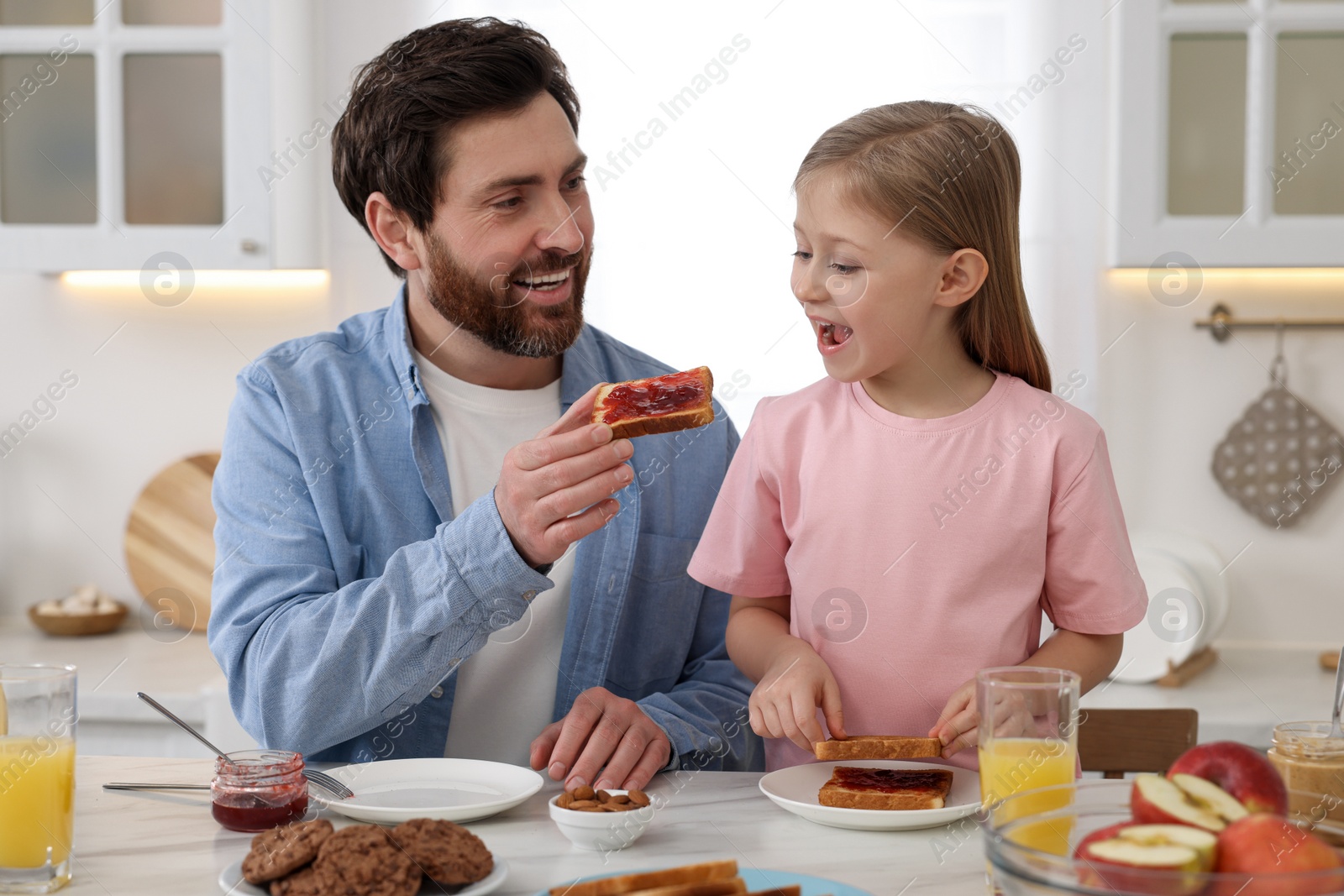 Photo of Father and his cute little daughter having breakfast at table in kitchen