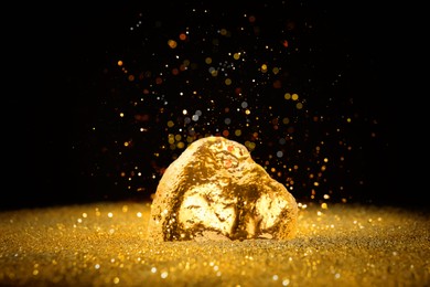 Image of Gold dust falling on gold nugget against black background