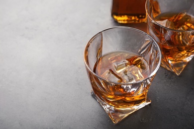 Photo of Golden whiskey in glass with ice cubes on table. Space for text