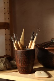 Photo of Set of different crafting tools and clay dishes on wooden table in workshop