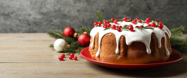 Image of Traditional Christmas cake decorated with glaze, pomegranate seeds, cranberries and rosemary on wooden table, space for text. Banner design