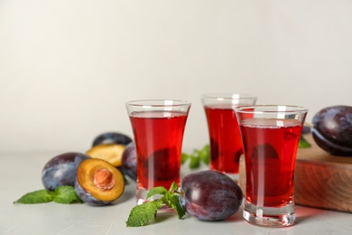 Photo of Delicious plum liquor, mint and ripe fruits on light table. Homemade strong alcoholic beverage