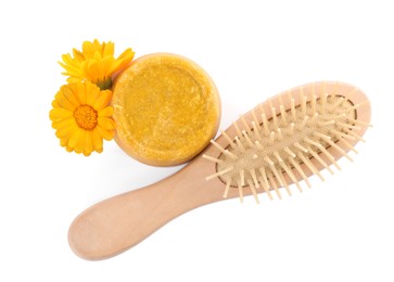 Photo of Yellow solid shampoo bar, hairbrush and flowers on white background, top view. Hair care