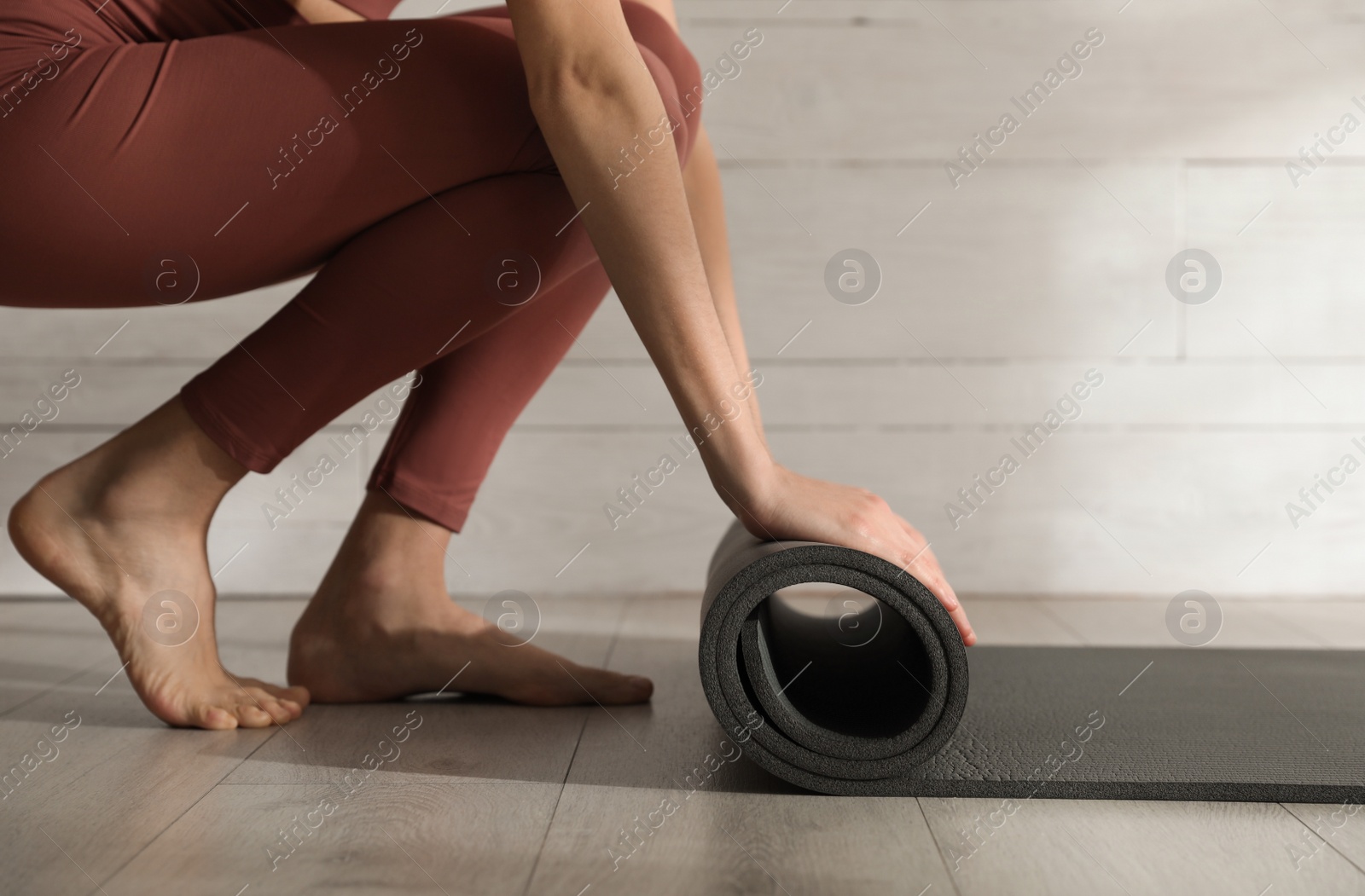 Photo of Woman rolling black yoga mat on floor indoors, closeup