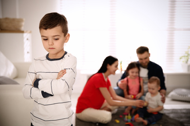 Photo of Unhappy little boy feeling jealous while parents spending time with other children at home