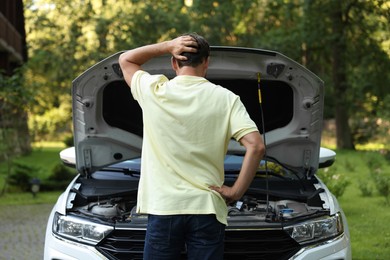 Photo of Man looking under hood of broken car outdoors, back view