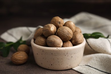 Photo of Whole nutmegs in bowl on brown table, closeup
