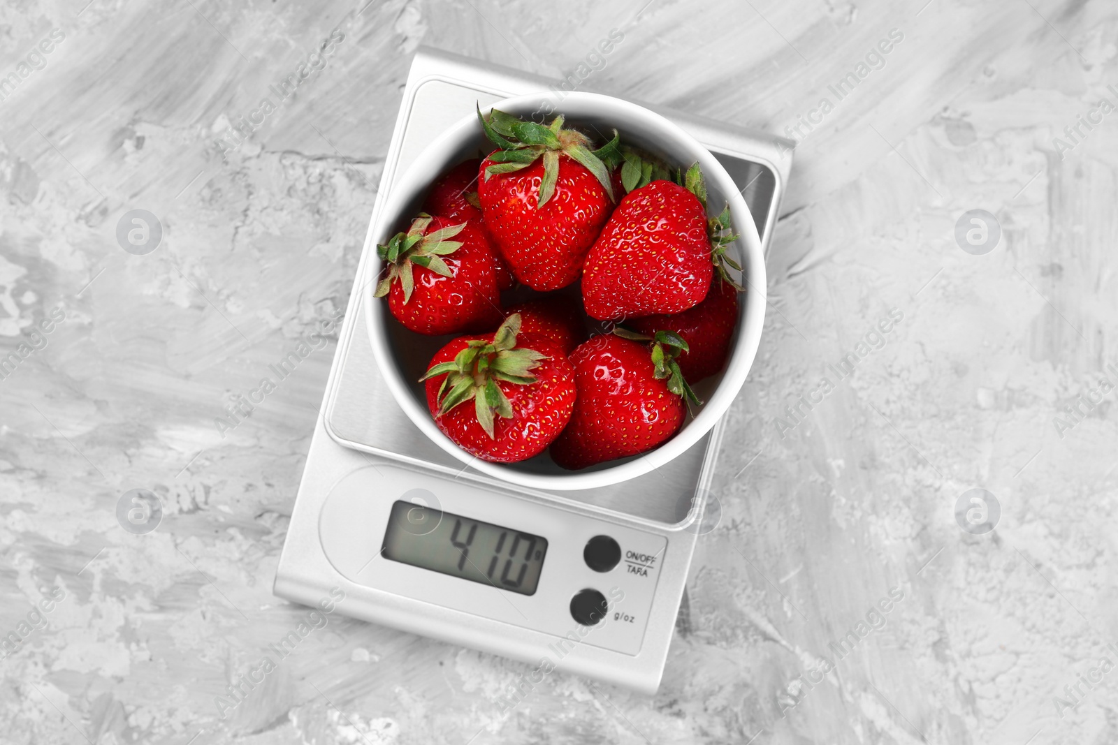 Photo of Kitchen scale with bowl of strawberries on grey textured table, top view