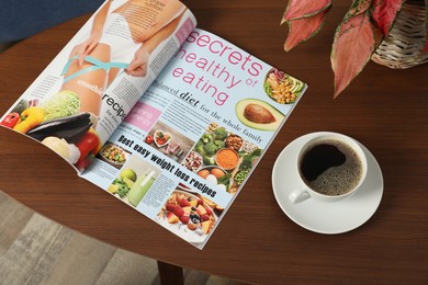 Photo of Open magazine, cup of coffee and houseplant on wooden table indoors, above view