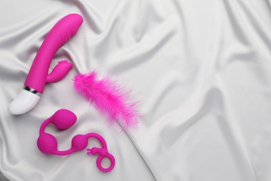 Photo of Pink sex toys and feather on white fabric, flat lay. Space for text