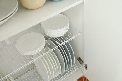 Photo of Clean plates, bowls and glass on shelves in cabinet indoors