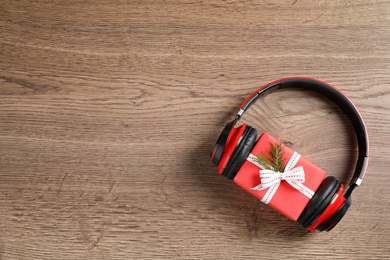Photo of Modern headphones and gift box on wooden background, top view with space for text. Christmas music concept