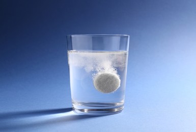 Photo of Effervescent pill dissolving in glass of water on blue background