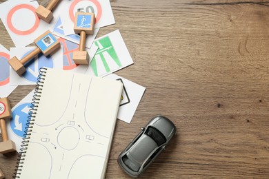 Photo of Many different road signs, notebook and toy car on wooden background, flat lay with space for text. Driving school