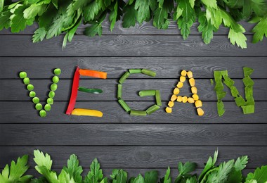Image of Word VEGAN made of different fresh tasty vegetables on grey wooden background, flat lay