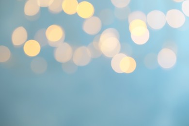 Photo of Blurred view of festive lights on light blue background, space for text. Bokeh effect