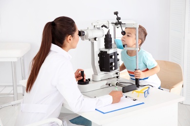 Photo of Children's doctor examining little boy with ophthalmic equipment in clinic