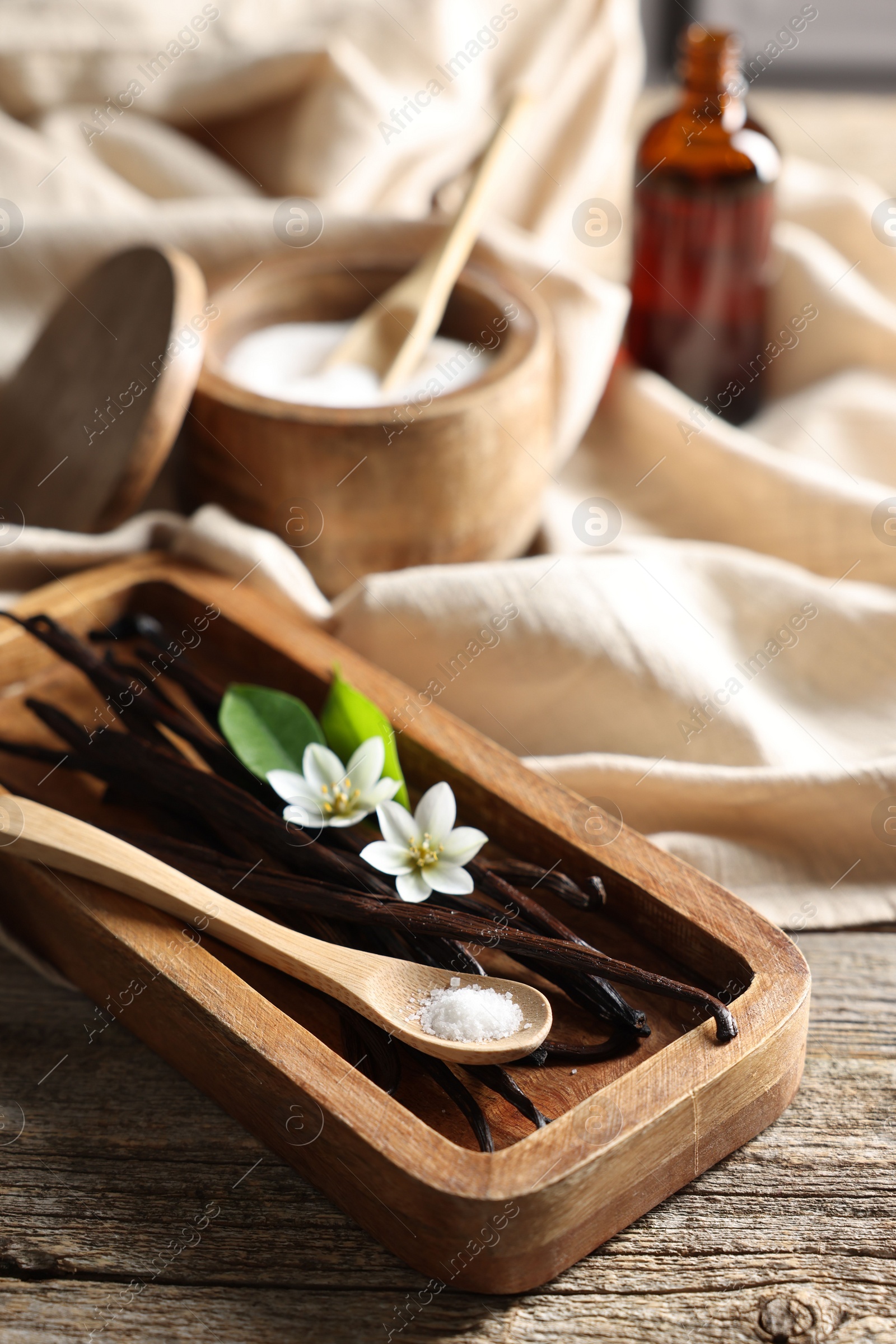 Photo of Vanilla pods, flowers, leaves and spoon with sugar on wooden table, closeup