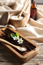 Photo of Vanilla pods, flowers, leaves and spoon with sugar on wooden table, closeup
