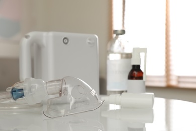 Photo of Face mask near nebulizer and medications on white table indoors. Inhalation equipment