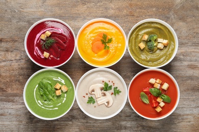 Photo of Various cream soups in bowls on wooden background, top view
